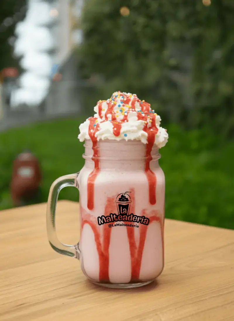 Malteada tradicional de fresa con crema batida, granillo de colores y salsa de fresa por el vidrio.